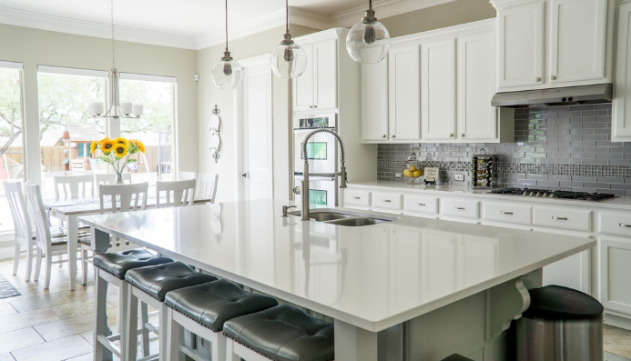 A kitchen with white cabinets and black stools.